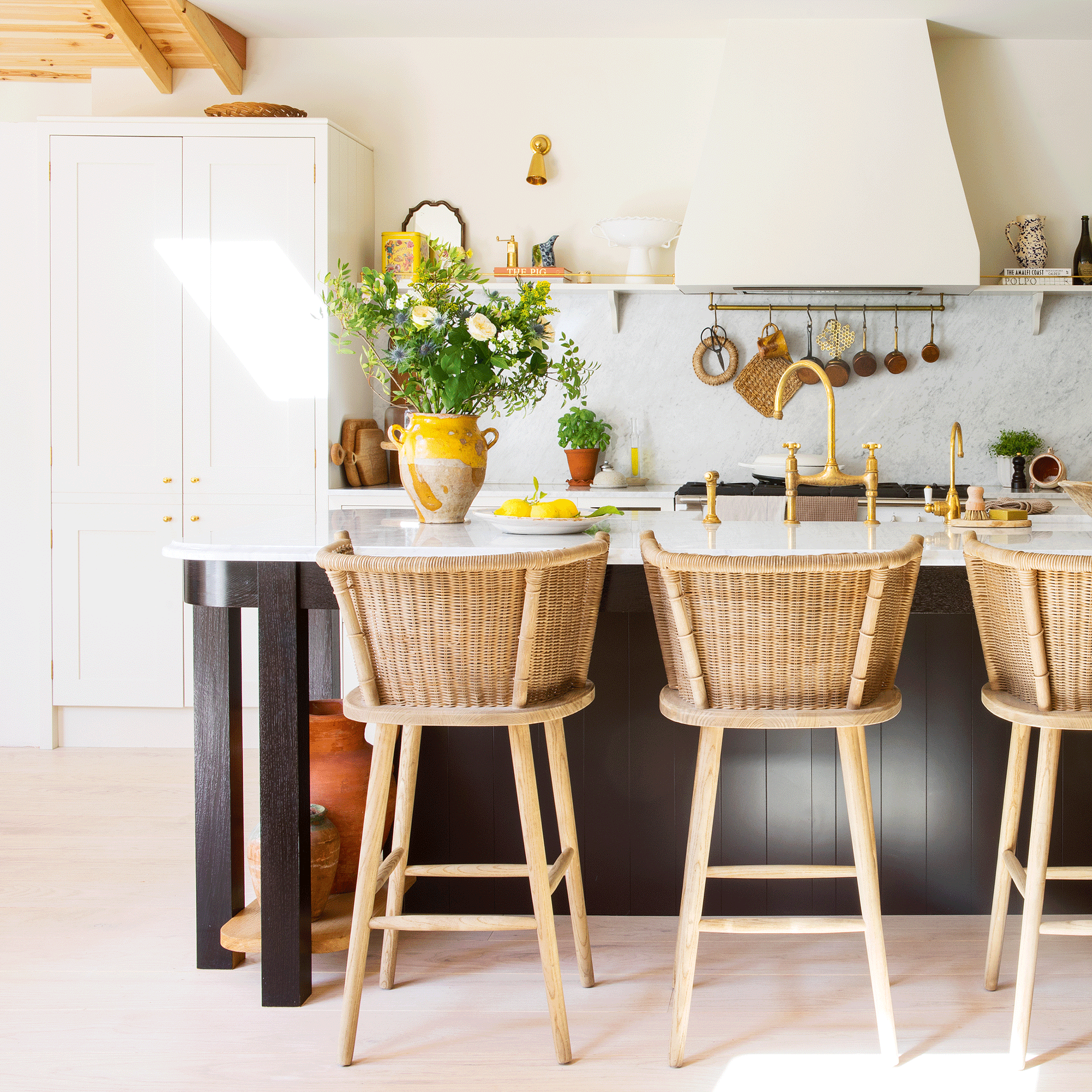 a large neutral open plan kitchen with a kitchen island with wicker bar stools and cream Shaker cabinetry