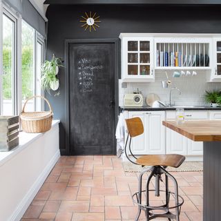 White kitchen cabinets with black wall and terracotta floor tiles