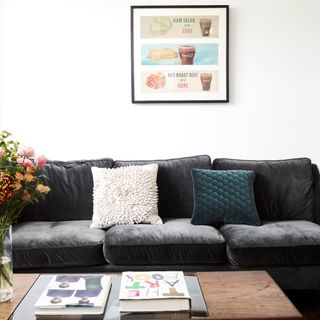 Dark sofa with white and navy cushion with hanging artwork, dark oak wood coffee table and books on top