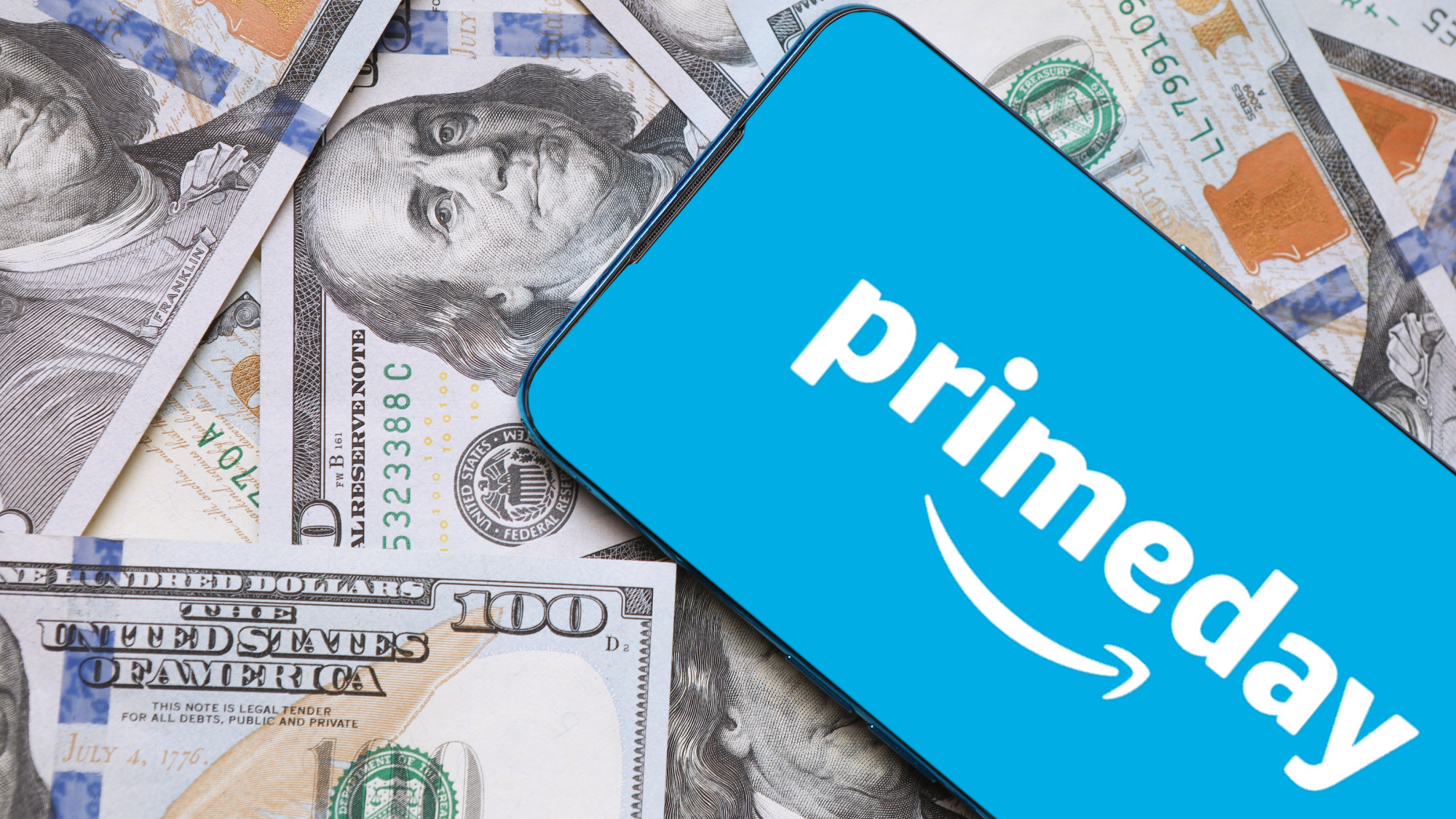 Smartphone displaying Prime Day on its screen with $100 dollar bills as the backdrop