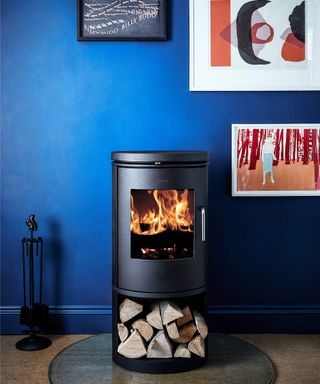 freestanding cylindrical log burner on glass hearth against wall painted bright blue