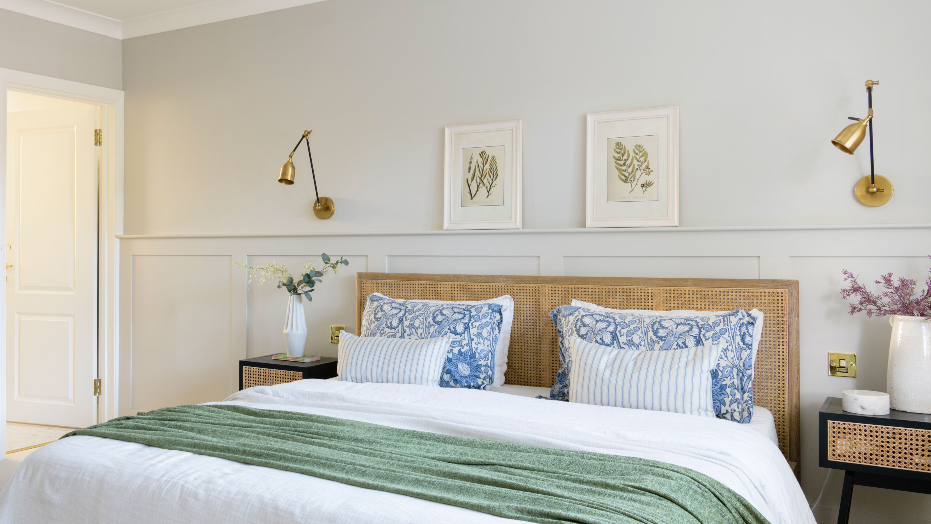 White bedroom with gold wall lights and rattan bed with white bedding and black and rattan bedside tables