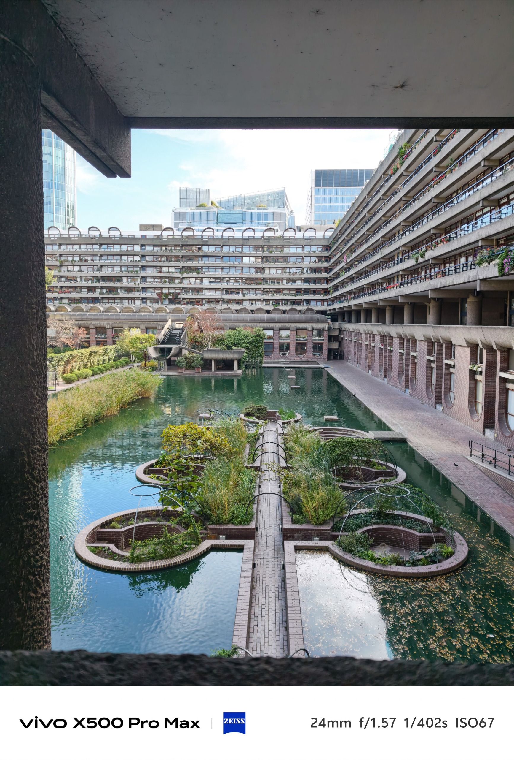 View across the Barbican lake and planted gardens toward surrounding brutalist residential buildings.