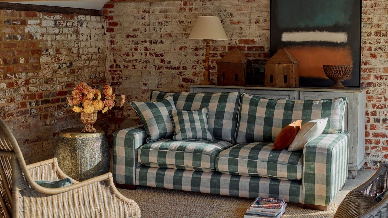 Checkered green white and blue Sofa in cottage style, small living room with exposed brickwork onwalls. There is sun shining in from the right and it looks cozy