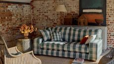 Checkered green white and blue Sofa in cottage style, small living room with exposed brickwork onwalls. There is sun shining in from the right and it looks cozy