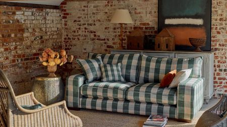 Checkered green white and blue Sofa in cottage style, small living room with exposed brickwork onwalls. There is sun shining in from the right and it looks cozy