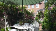 Charming garden patio area featuring antique-style outdoor furniture and a green parasol
