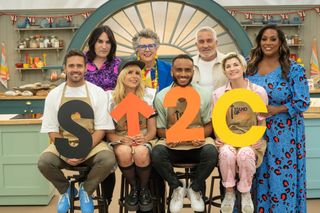 Noel Fielding, Prue Leith, Paul Hollywood and Alison Hammond stand behind Spencer Matthews, Paloma Faith, Munya Chawawa and Jodie Whittaker holding up the Stand Up to Cancer logo in the tent for The Great Celebrity Bake Off for Stand Up to Cancer.