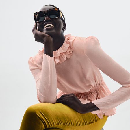 Model wearing a peach ruffle collar top and gold trousers sold at Mytheresa