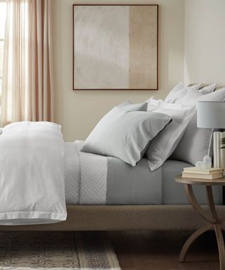 Side view of gray and white bedding on a bed against cream walls.