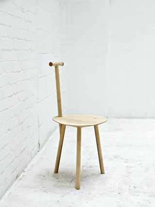 Three-legged wooden chair with a slim backrest photographed against white background