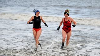 Two women leaving the sea wearing neoprene boots and gloves