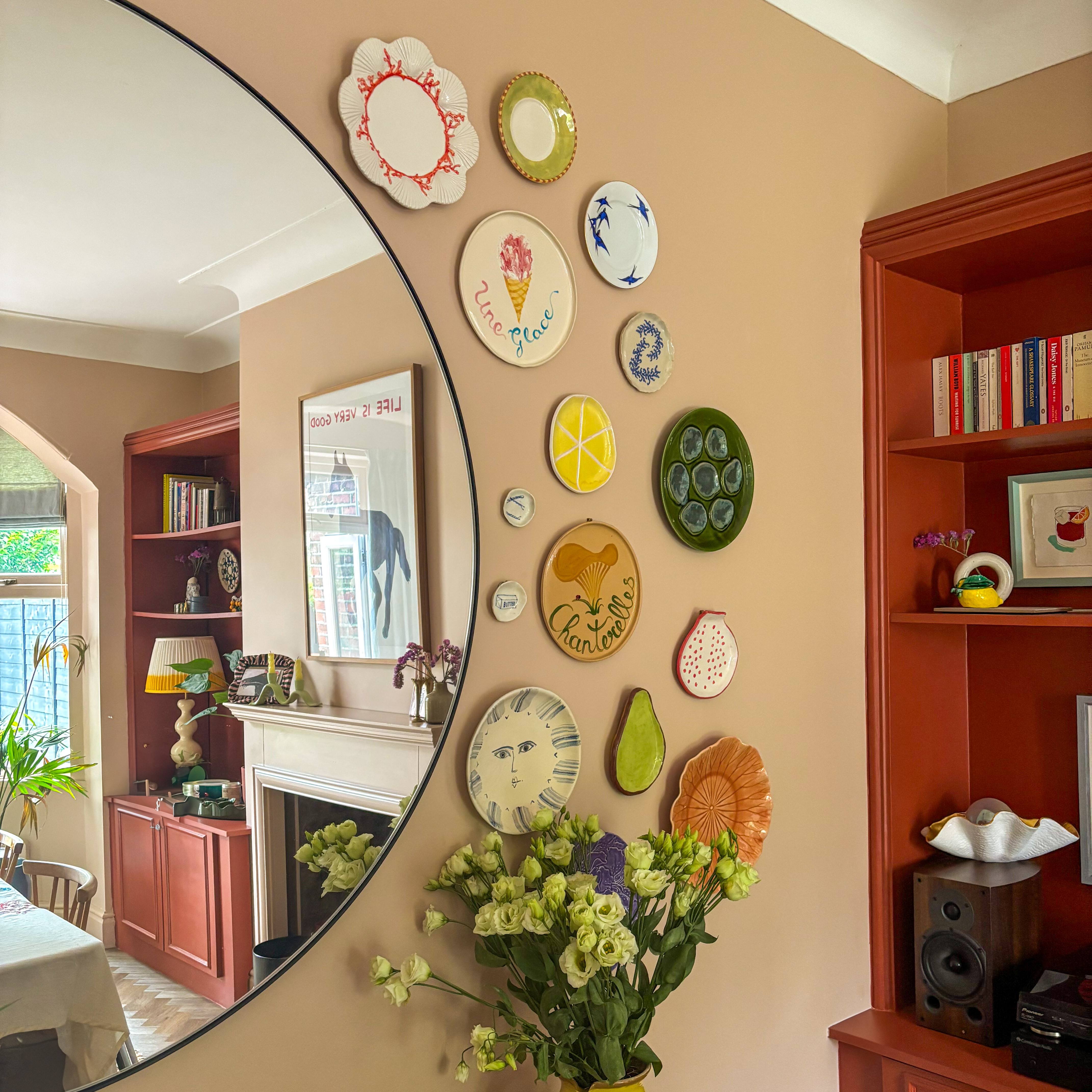 vintage plates on a beige wall around a large round mirror