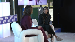 Asha Sharma speaks on stage during a Fortune Conversations interview, discussing Xbox's Project Helix strategy while seated in a white chair opposite the event moderator.