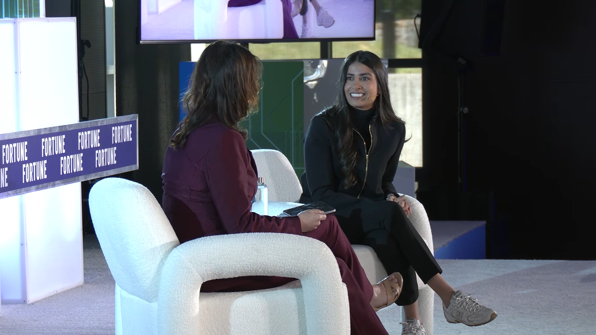 Asha Sharma speaks on stage during a Fortune Conversations interview, discussing Xbox's Project Helix strategy while seated in a white chair opposite the event moderator.