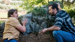 Javi (Pedro Pascal) and Nick Cage (Nicolas Cage) hide behind a rock in "The Unbearable Weight of Massive Talent".