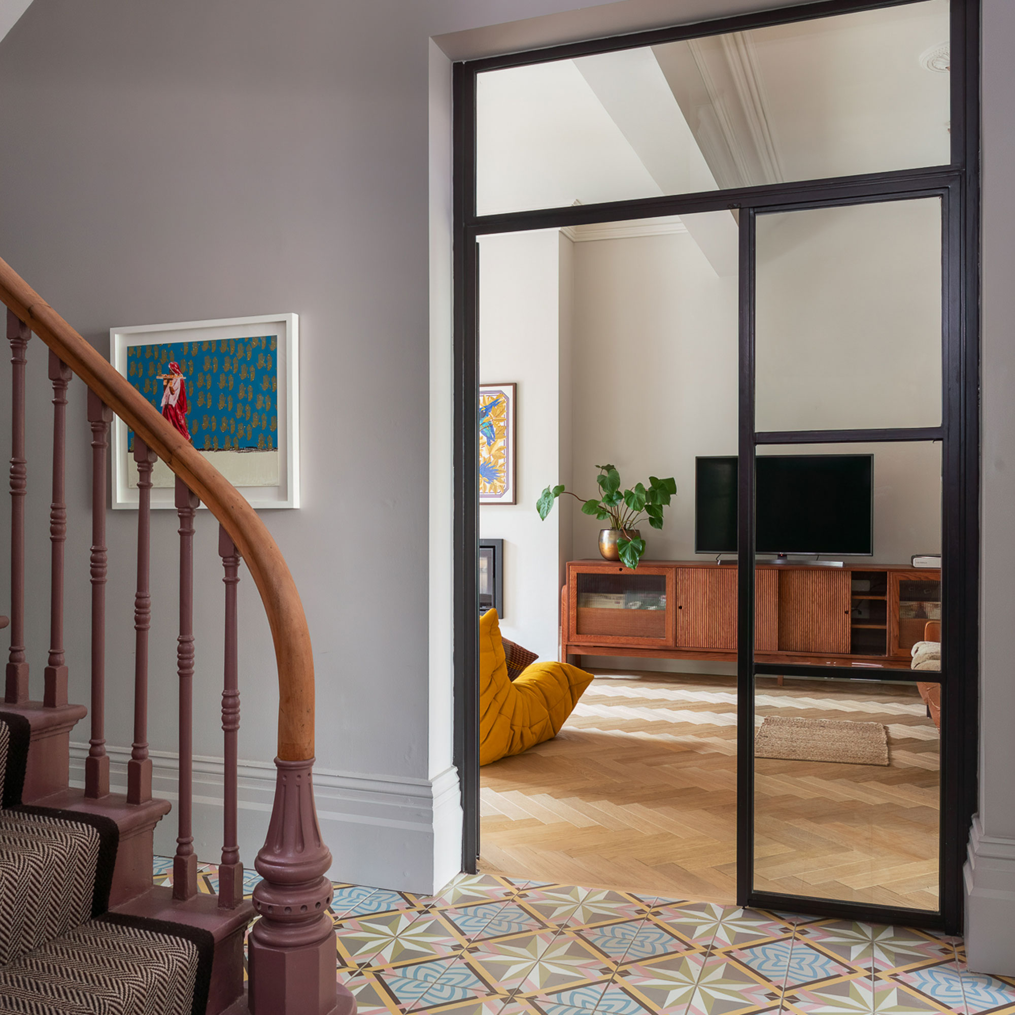hallway with patterned floor tiles and glass internal doors leading to snug with herringbone wooden flooring