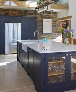 Dark hued kitchen island with plug socket and glass-fronted doors for glassware