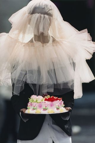 Man in Simone Rocha veil and suit holding white cake
