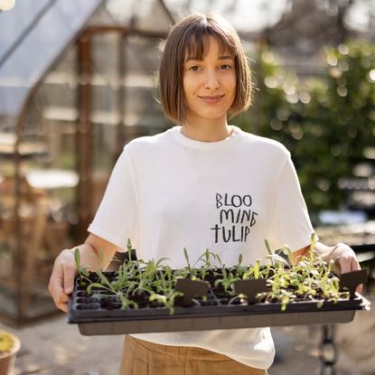 A young woman holds a tray of seedlings