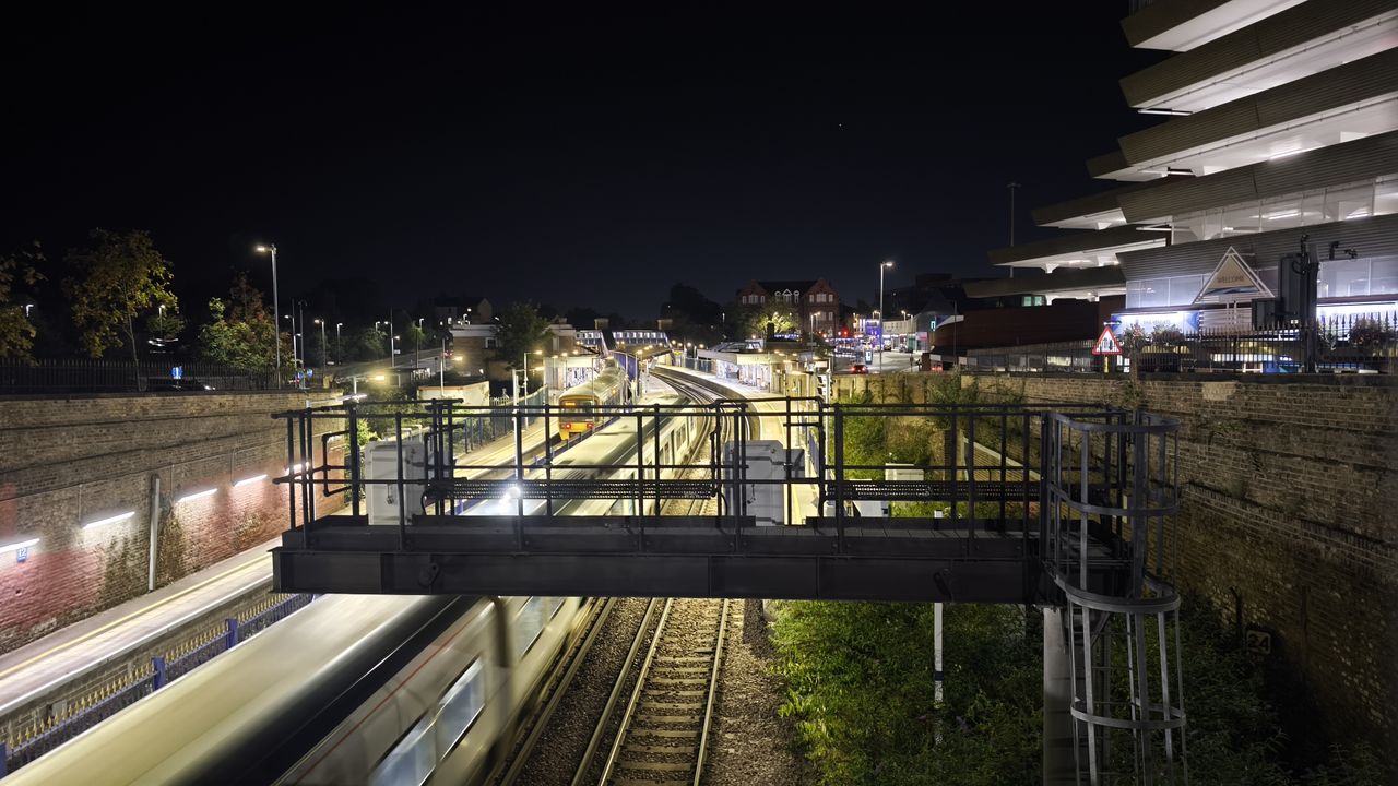 Night photo of a train station with three platforms, one train is passing through the station while another sits stationary on the left-most platform