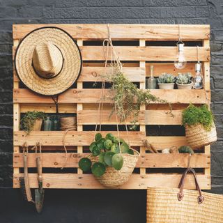 Hats and wicker planters hanging from wooden trellis with garden tools and light bulbs