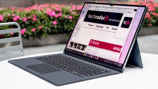 En Samsung Galaxy Tab S9 Ultra står åpen med et tastatur på et hvitt bord utendørs, med TechRadars nettside på skjermen.