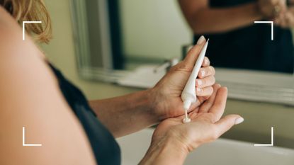 View of woman&#039;s hands squeezing sunscreen onto hands in front of restroom mirror, representing the question of what SPF sunscreen should I wear on my face every day