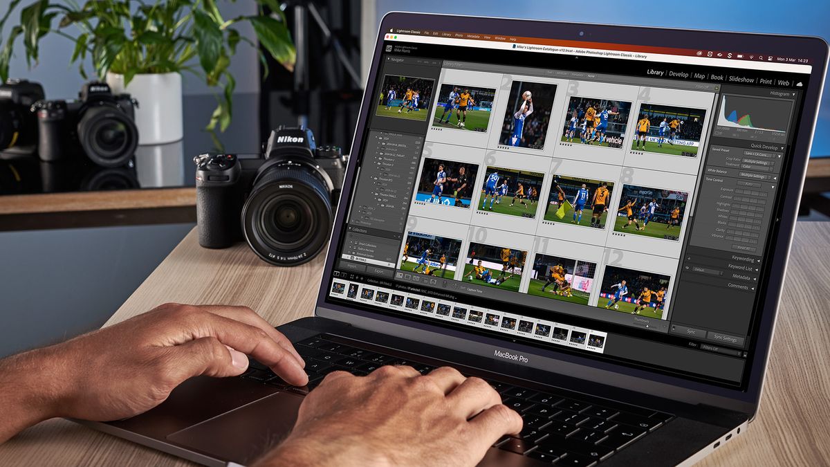 Hands typing on MacBook running Adobe Lightroom Classic in Library module with images of footballers. A few cameras can be seen in the background as well as a pot plant 