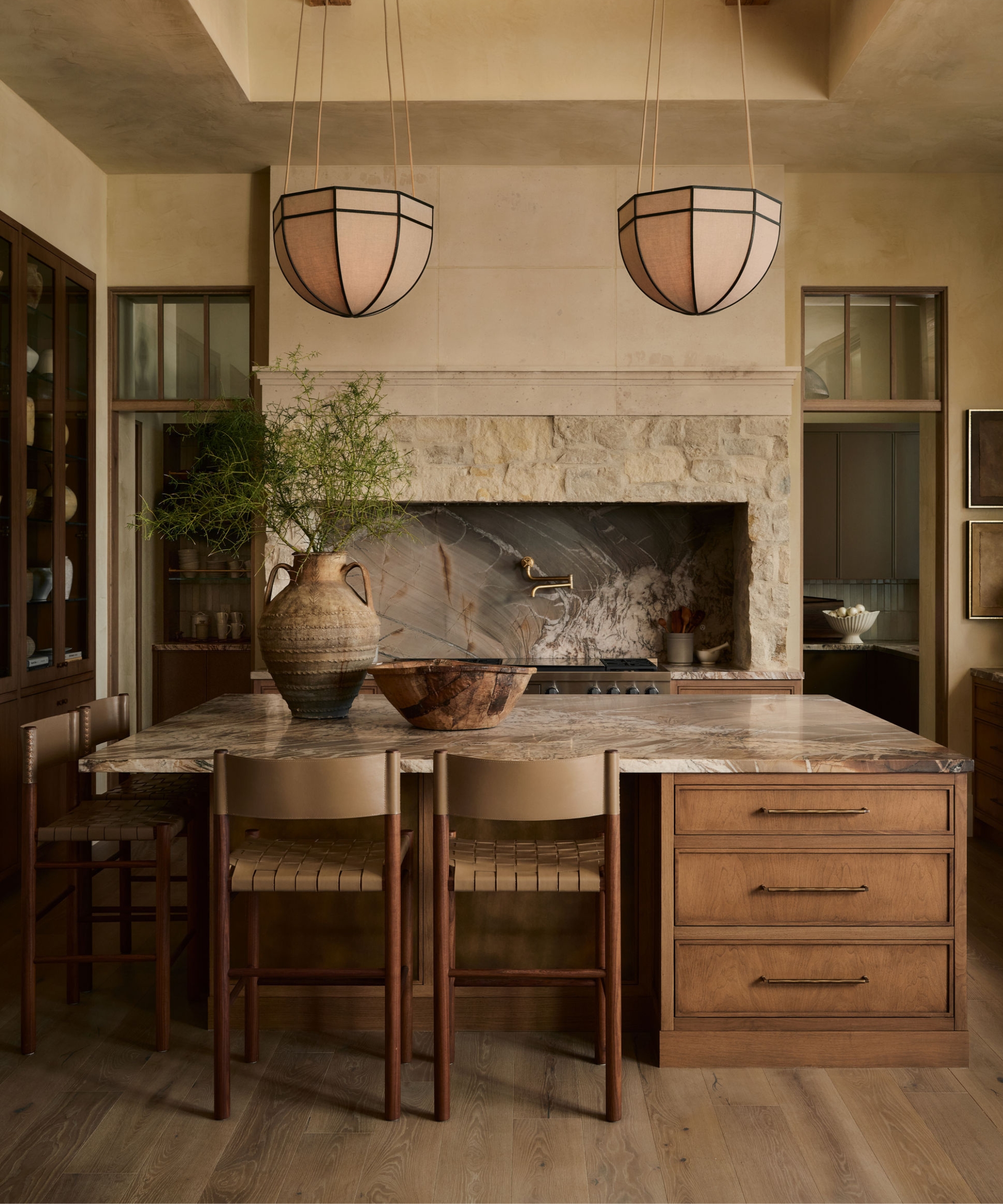 A warm neutral kitchen with a wood island, stone countertops, and a stone range surround