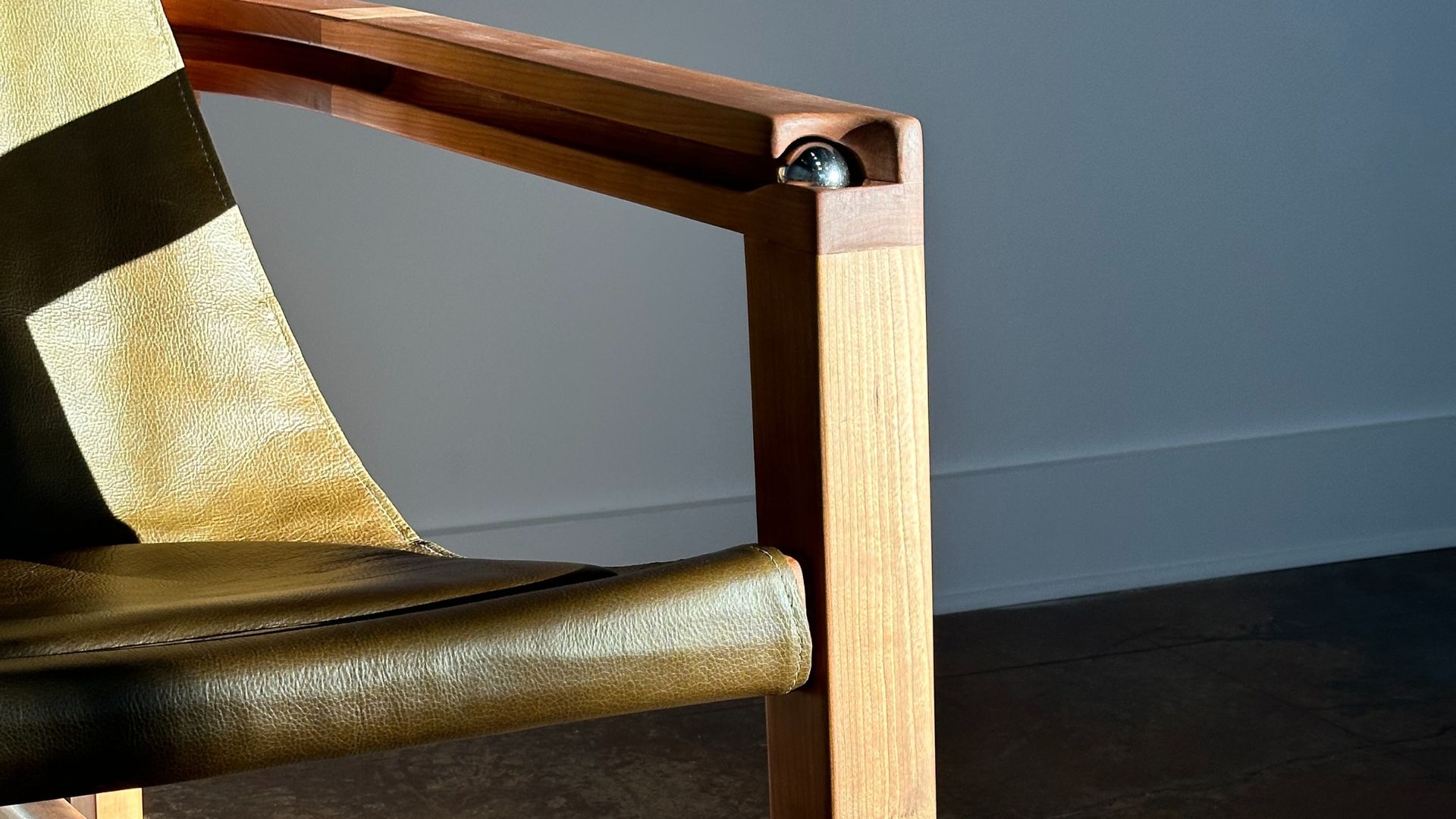A close-up of a cherry wood chair with green leather and a steel ball in the arm