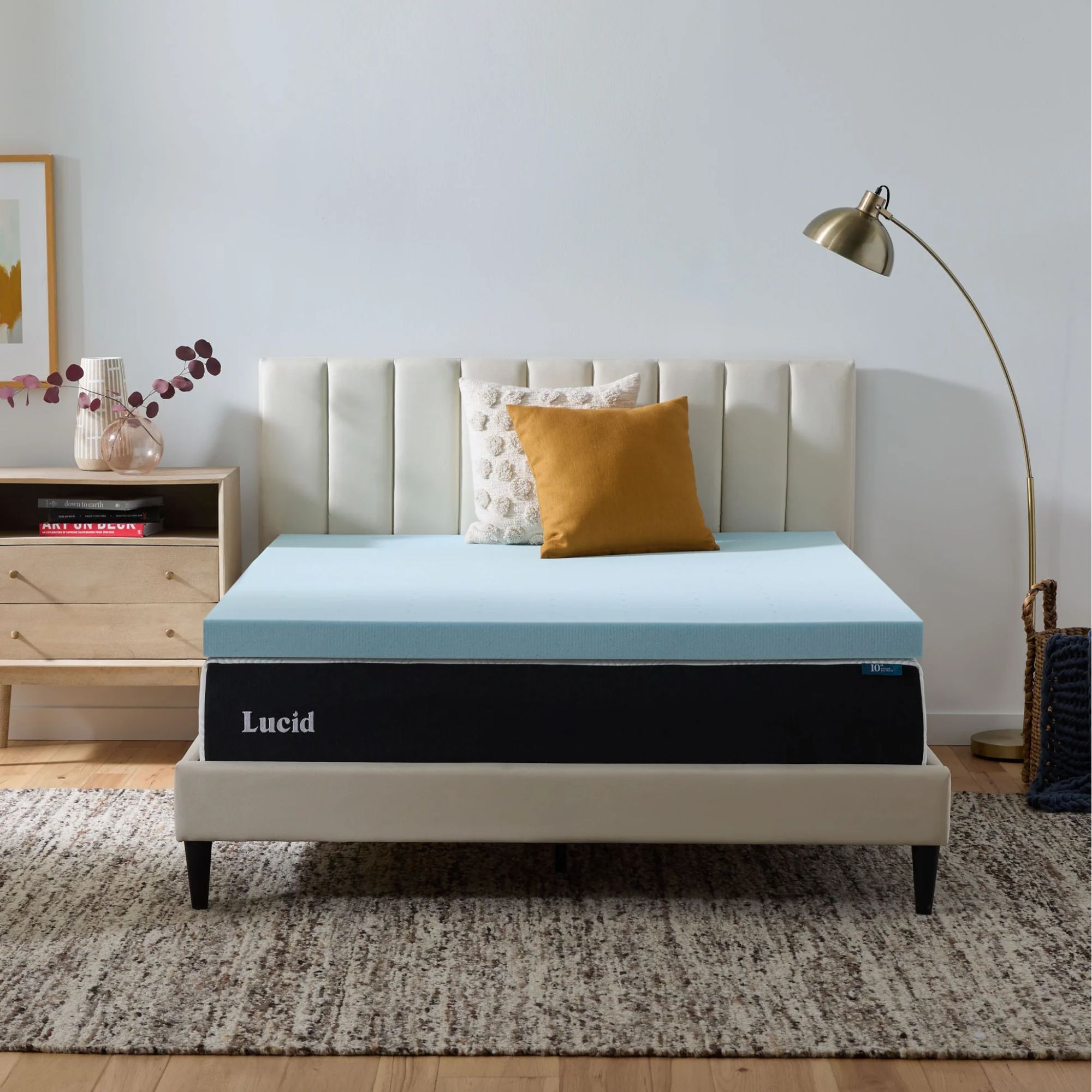 A blue Lucid mattress topper on a white fluted bed in a white bedroom with light wood flooring and large rug.