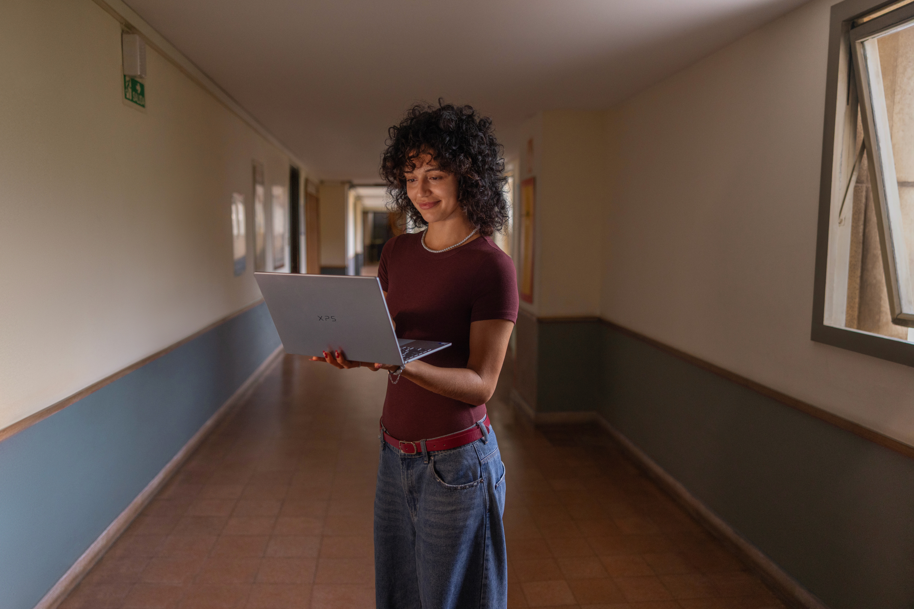 Person holding an XPS 13 laptop in a sunlit hallway.