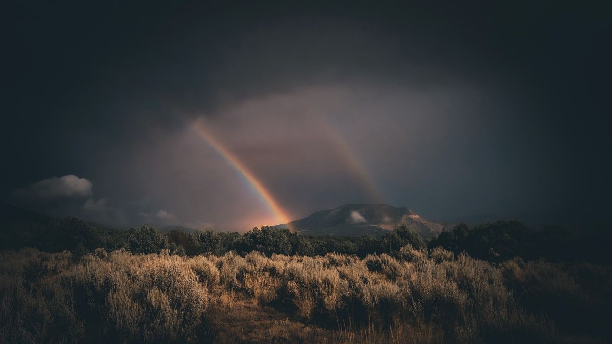 a faint but colorful double rainbow rises out from the landscape into a cloudy sky. 