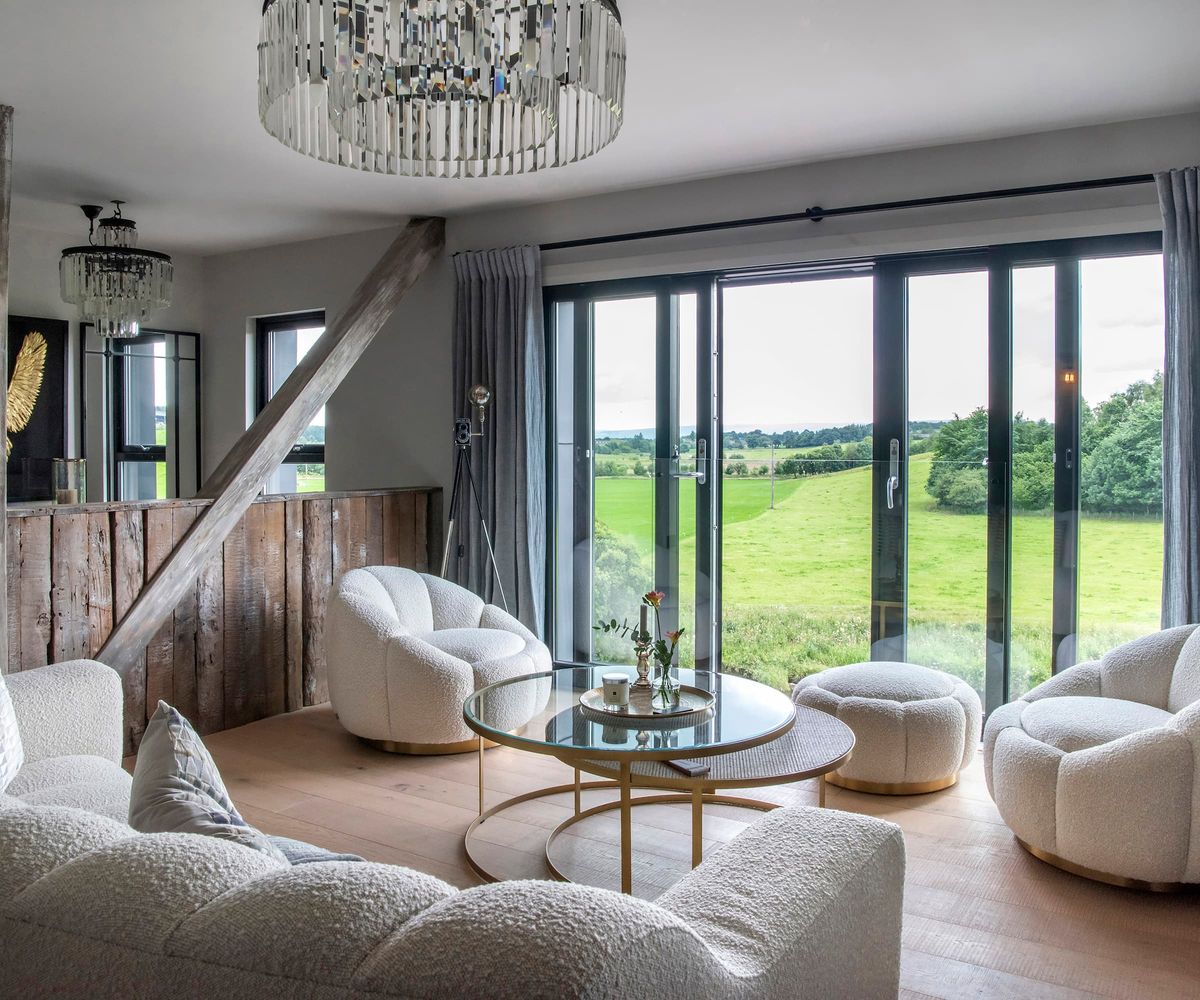A sitting room with a chandelier and bifold doors with white sofas