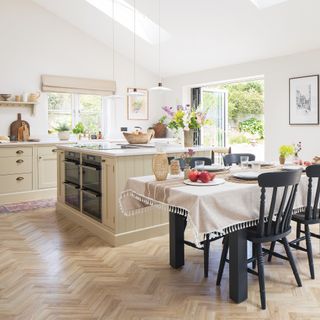 country cottage kitchen with cream coloured shaker cabinets and cup handles, kitchen island with two built-in ovens, charcoal coloured dining table and chairs