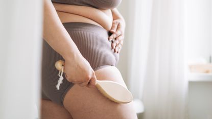 Close up view of the back of a woman while she uses a body brush on her upper thigh