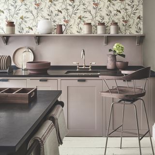 lilac kitchen with open shelving, white painted floor boards, bar stool, black worktops, wallpaper with birds, artisan pots