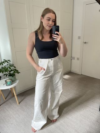 Woman wears grey tank top and white jeans