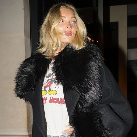 Elsa Hosk wears a black fur coat, mickey mouse graphic t-shirt, jeans, black pumps, and a white hermes bag.