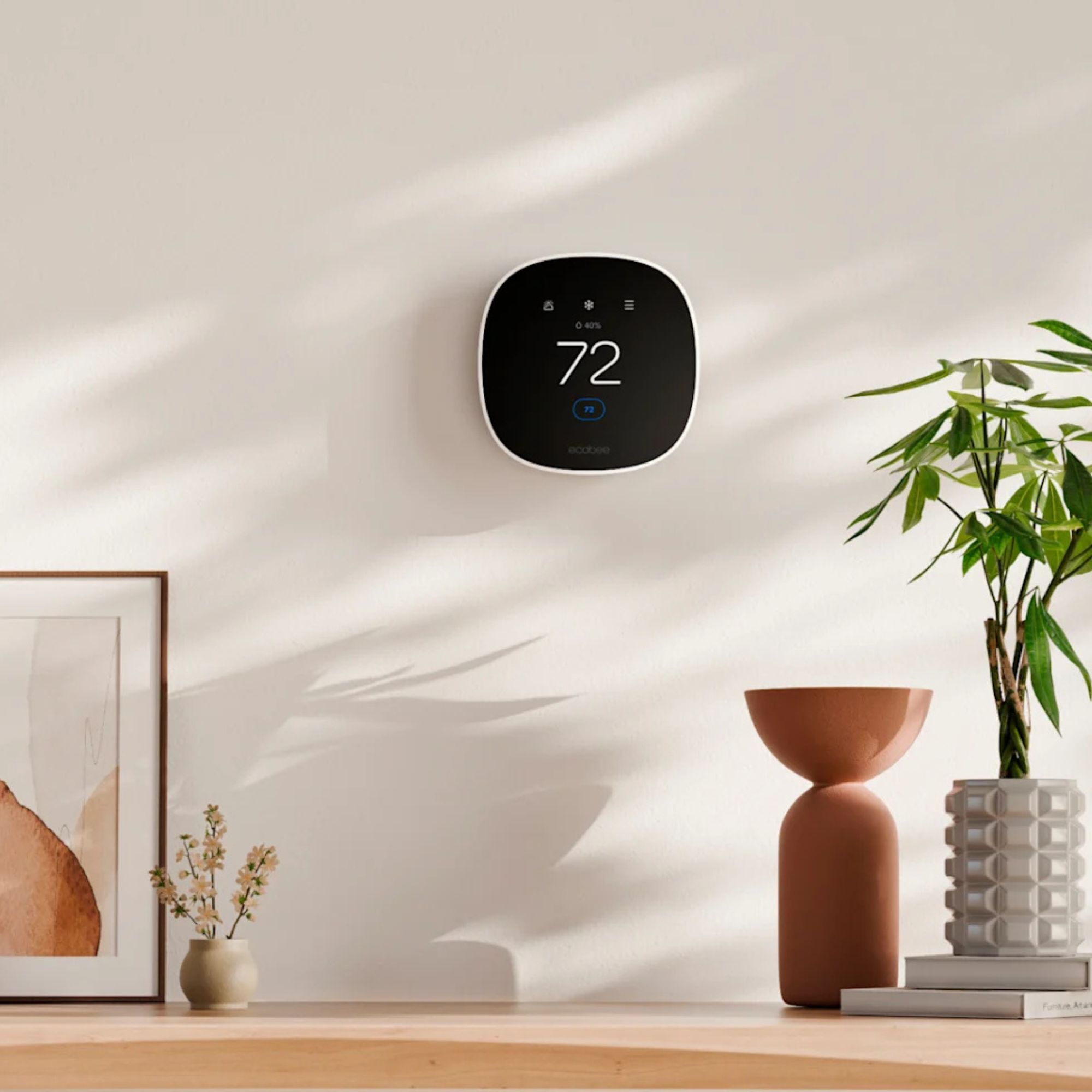 ecobee Smart Thermostat on white wall, pictured in front of vases and flowers with shadowy sunbeams pictured across wall.