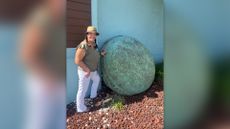 We see a woman standing outside a building next to a large circular green drum-shaped object. 