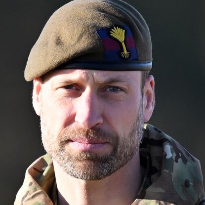 Prince William wearing a camo coat and green beret looking into the camera