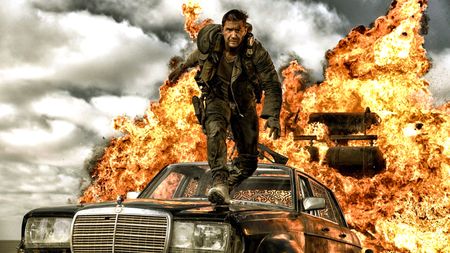 Max Rockatansky (Tom Hardy) stands on the hood of a car with an explosion behind him in a promotional still for Warner Bros. "Mad Max:Fury Road"