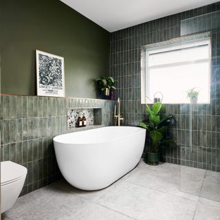 a dark green bathroom with dark green tiles and dark green painted wall, a large white bathtub and a decorative framed print on the wall