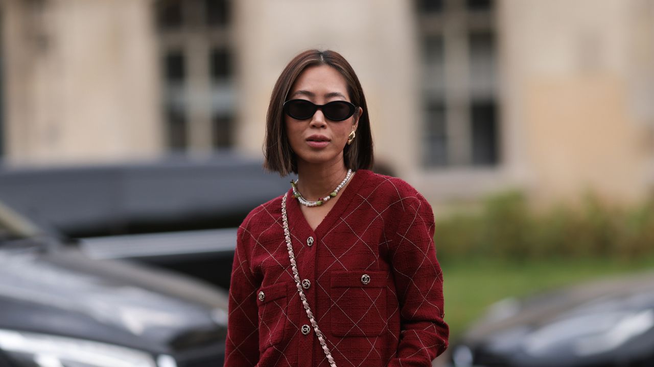 Aimee Song is seen outside Chanel show wearing black Chanel sunnies, golden earrings, a burgundy colored Chanel set consisting of jacket and short skirt, red and white tweed Chanel checkered Flap Bag and black Chanel lace-up heels during the Womenswear Spring/Summer 2024 as part of Paris Fashion Week on October 03, 2023 in Paris, France