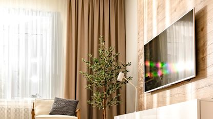 A wall-mounted TV in a living room reflecting a sharp beam of sunlight coming through a window in the background