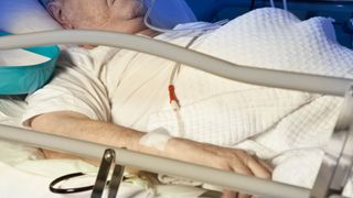 elderly man laying in a hospital bed with an IV in his arm
