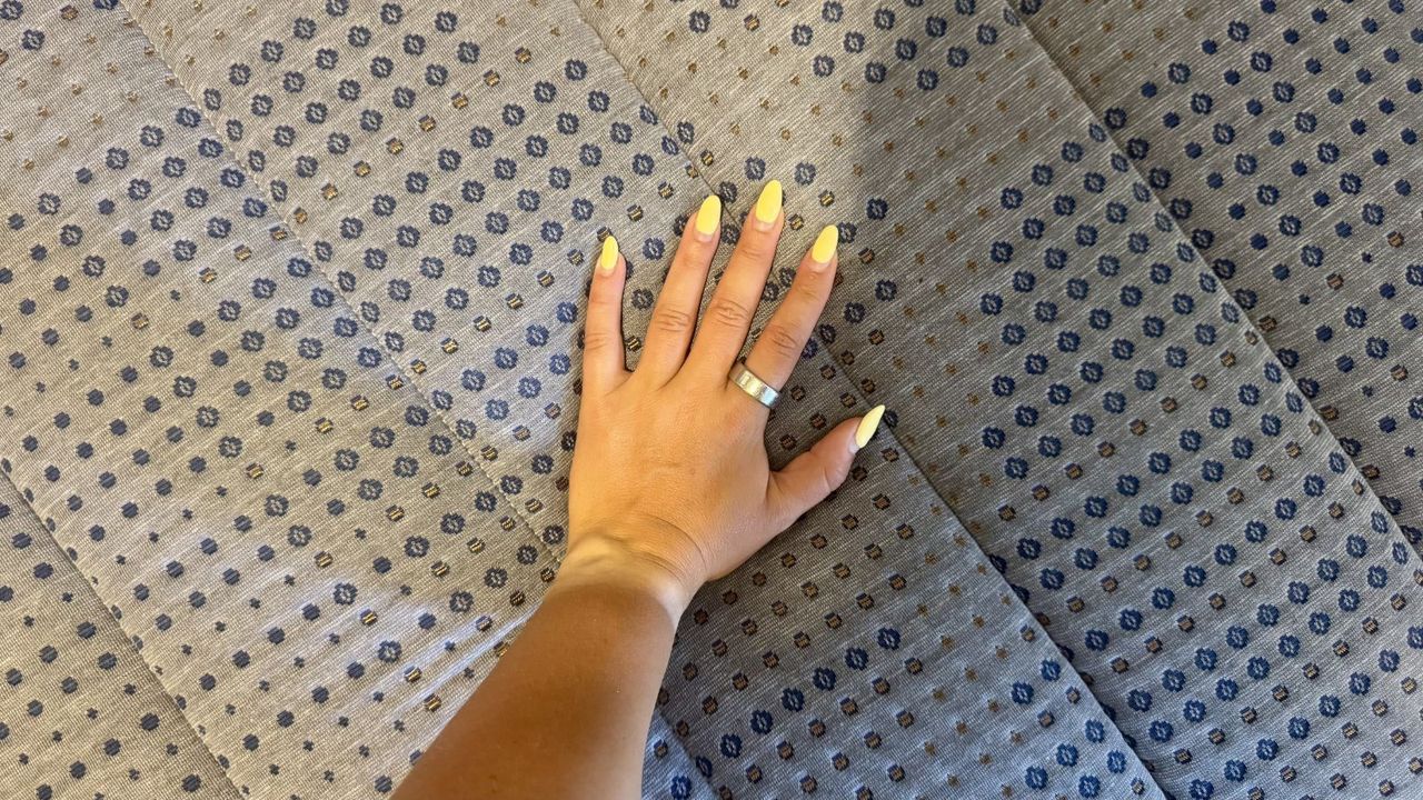 A woman's left hand with yellow nails wearing a silver Oura Ring 4 on index finger pressing into grey and navy patterned cover of Brooklyn Bedding Copperflex mattress