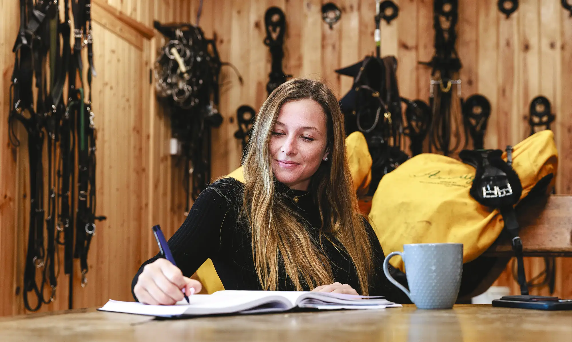 Cosby Green sat at a desk writing with bridles hung behind